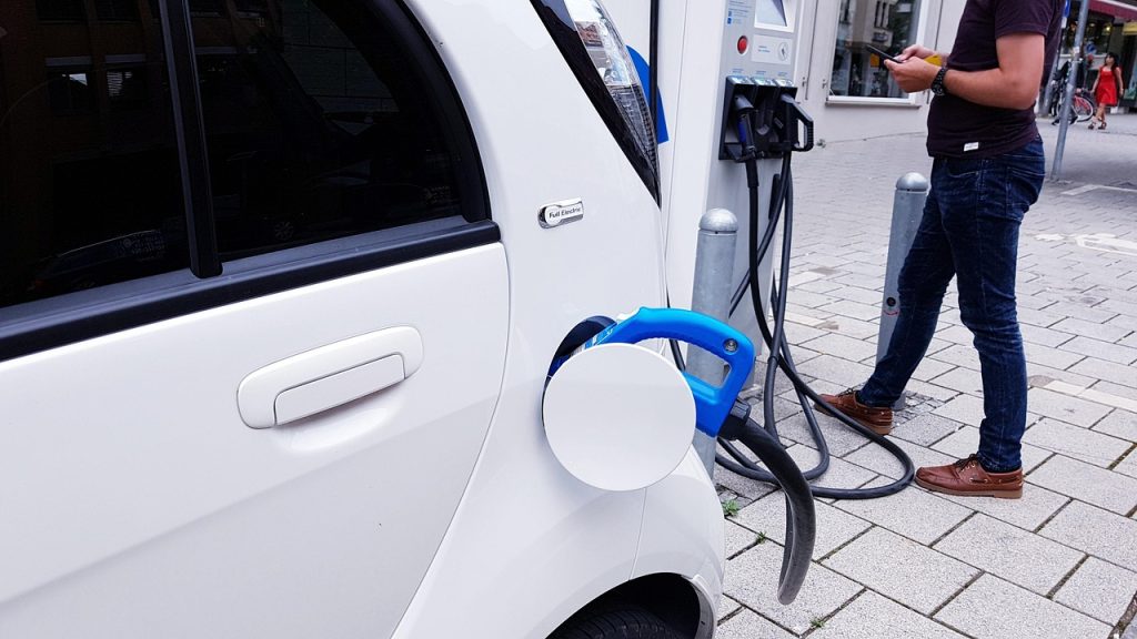 Homme branchant un câble de recharge sur une voiture électrique blanche