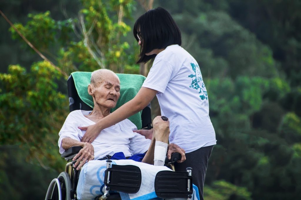 Jeune aidante posant la main sur l'épaule d'un homme âgé en fauteuil